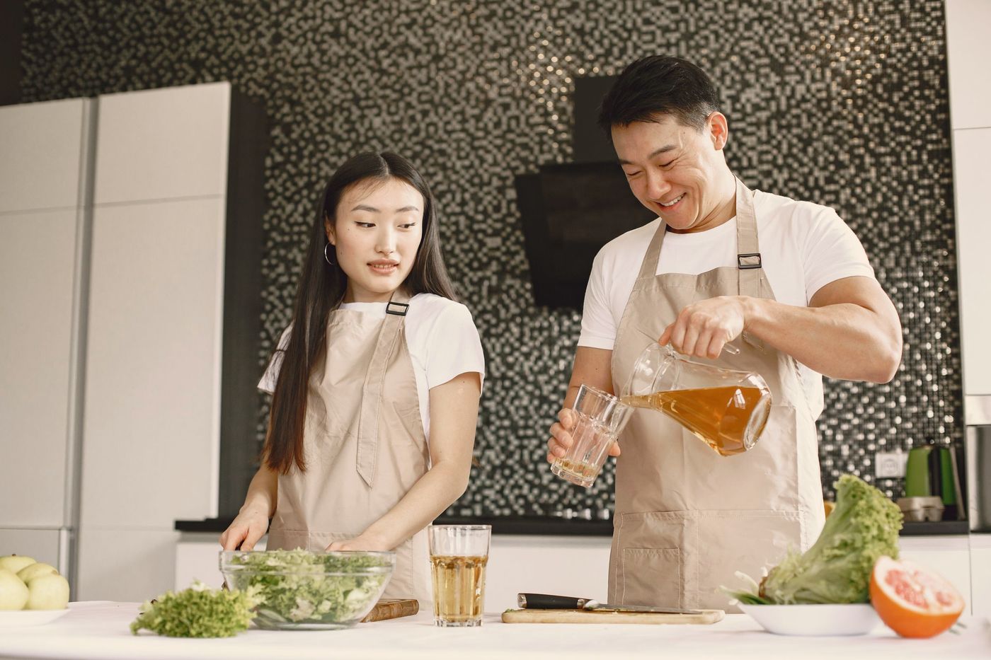 一对亚洲情侣在洒满阳光的厨房里一起做饭，笑成一团