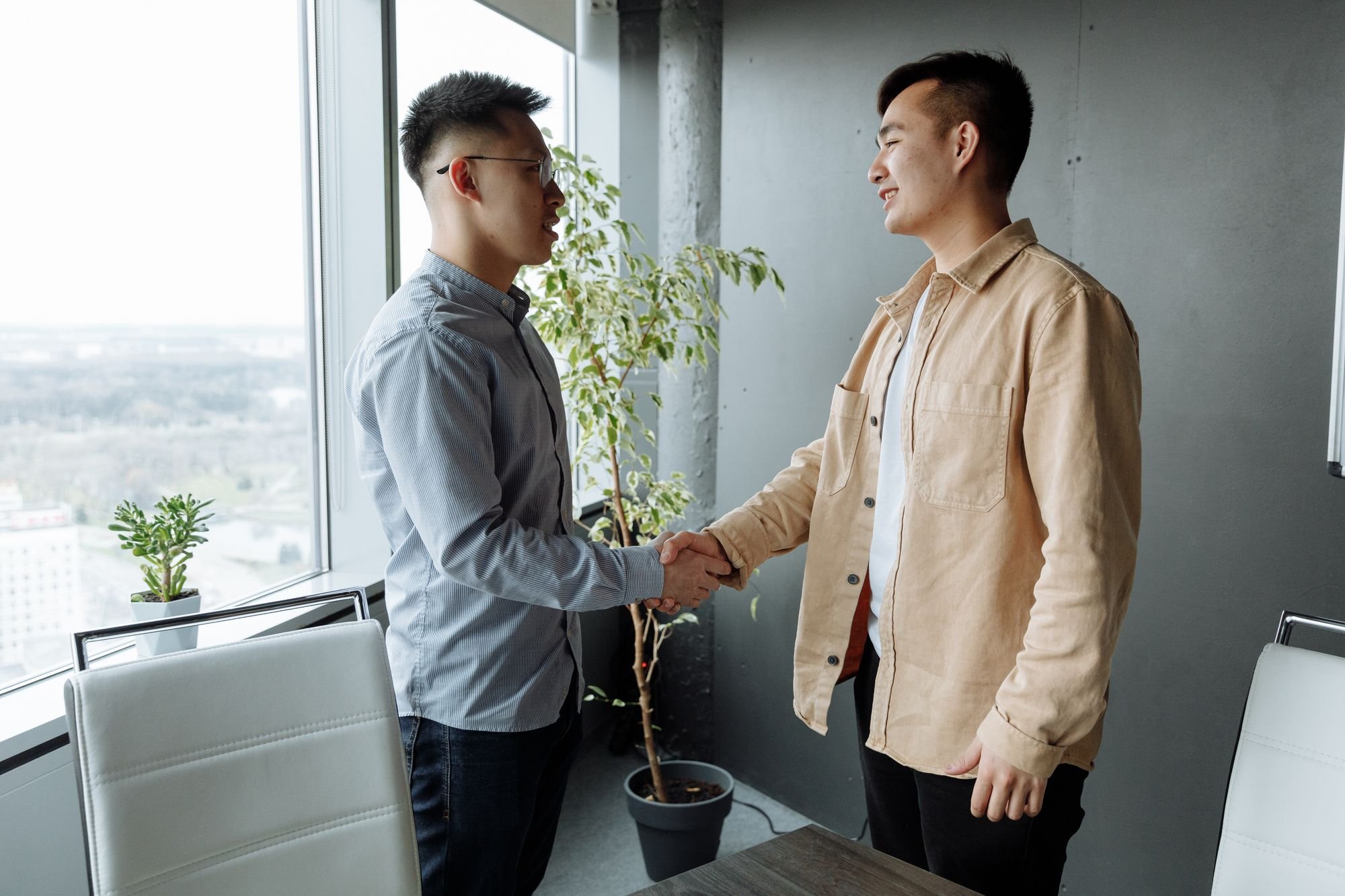 两位年轻的亚洲职场人士在明亮的办公室里握手微笑